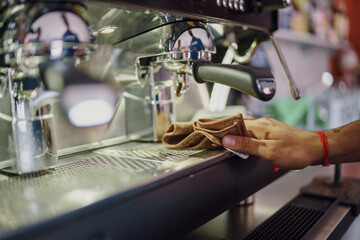 Close up shot of a barista cleaning a professional espresso machine with a cloth in a cafe...