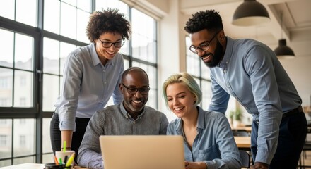 A diverse group of four smiling business professionals collaborating and looking at a laptop screen in a bright, modern office environment.