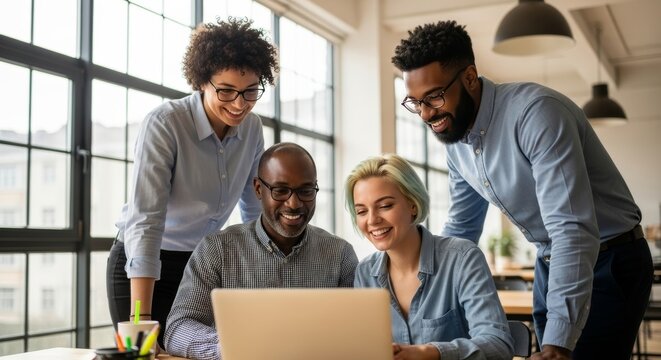 A diverse group of four smiling business professionals collaborating and looking at a laptop screen in a bright, modern office environment.