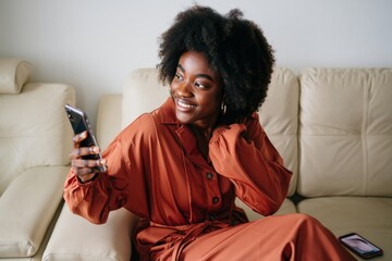 Beautiful african american woman using smartphone on sofa at home in living room