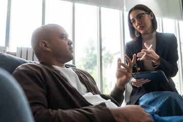 Asian man consulting with asian woman psychologist at mental health clinic. psychologist taking notes and talking with male patient with depression. © BJ Day Stock