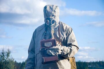 Military dosimetrist measures radiation on a grassy area. chemical protective SUIT and gas MASK,...