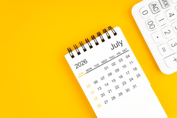 July 2026 calendar and calculator on yellow background, Flat lay.