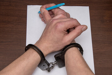 A man in handcuffs writes on paper with a blue pen, symbolising limited freedom of speech.