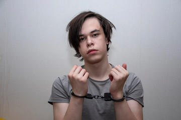 A handcuffed teenager sits on a grey background. Juvenile delinquent, criminal liability of minors....