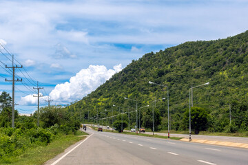 Beautiful view of asphalt highway road with electric pole and green mountain with sky clouds. Landscape with curved roadway through mountain pass in spring. Journey in nature mountain road. Travel.
