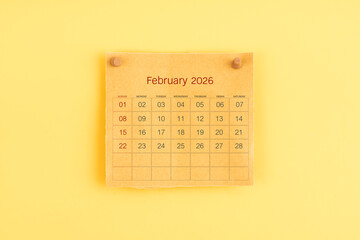 February 2026 brown calendar with wooden thumbtack on yellow color background.