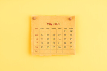 May 2026 brown calendar with wooden thumbtack on yellow color background.