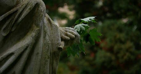 Close-up of a marble statue holding a green leafy branch, surrounded by a dark, forested background