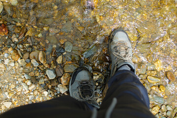 A Latino adult man has his gray leather boots in the creek to cool off after having walked in the forest for a few good hours, this man is dressed in gray pants.
