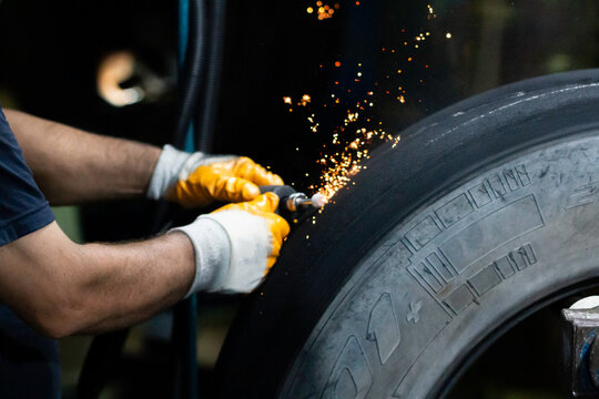 Tire retreading master cleans the wounds of the truck tire coming out of the rasping machine with a grinder.