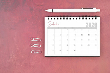 Desk calendar for September 2026 and pen with paper clips on red table, Flat lay.