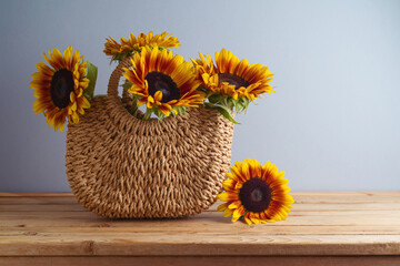 Sunflowers in straw fashion bag on wooden table