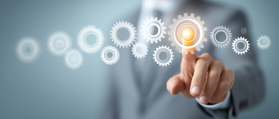 Fototapeta premium A person in business attire interacts with a glowing gear icon among multiple transparent gears, symbolizing technology, innovation, and system management