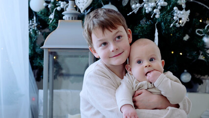 Two young brothers are standing in front of a festive christmas tree, savoring the holiday season with their family. A day with family before Christmas. New Year's Eve with family