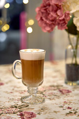 A Warm Glass of Coffee with Frothy Cream Set Against a Charming Floral Background, Perfect for Cozy...