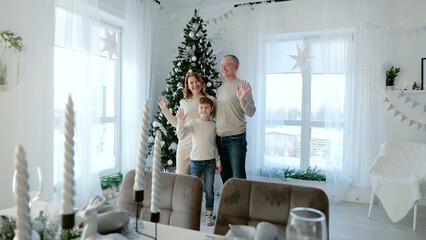 Family poses in festive living room with christmas tree in background, waving and smiling at camera. A day with family before Christmas. New Year's Eve with family