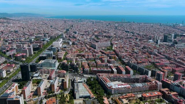 Wide drone view of Barcelona as Avinguda Diagonal leads across the Eixample grid to the Mediterranean coast. Sunny cityscape for travel, urban planning and real estate stories.