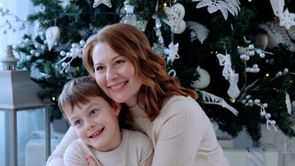 Mother and her son savor the festive christmas ambiance next to their exquisitely adorned holiday tree. A day with family before Christmas. New Year's Eve with family