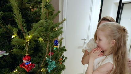 Mother and daughter standing near sparkling christmas tree, gazing at ornaments, sharing warm family moment during festive holiday celebration
