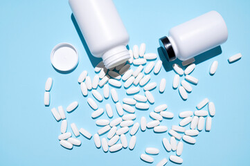 White container, plastic packaging and scattered white tablets, vitamins, pills, food supplements on blue background top view. Medical and pharmaceutical concept, health concept