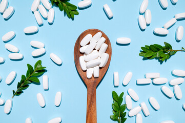 White tablets, vitamins, pills and green leaf in wooden spoon on blue background top view. Medical pharmaceutical background, health concept, organic dietary supplements, self care