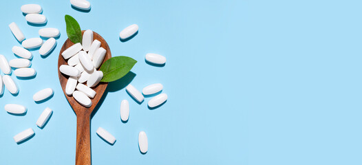 White tablets, vitamins, pills and green leaf in wooden spoon on blue background top view. Medical pharmaceutical background, health concept, organic dietary supplements, self care