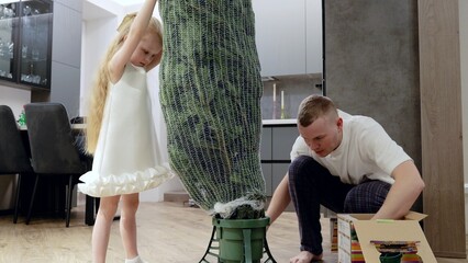 Father and daughter carefully unwrapping festive christmas tree, sharing warm holiday moments in decorated living room filled with seasonal joy and anticipation