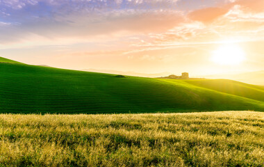 countryside sunset in green hills of spring fields with old castle farm and mountains on background of evening landscape