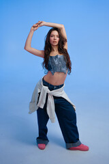 Young woman striking a dynamic pose on a blue background indoors