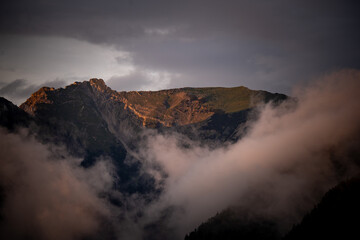 Obraz premium Dramatic Alpine Sunset: Golden Light on Rugged Peaks & Misty Clouds – Majestic Mountain Landscape