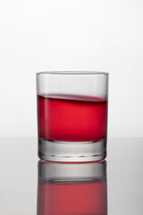 Old fashioned drinking glass containing bright red liquor, isolated on white background with reflection and bokeh