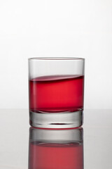 Old fashioned drinking glass containing bright red liquor, isolated on white background with reflection and bokeh
