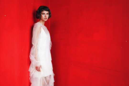 Model poses elegantly in modern fashion against a bold red wall during a photoshoot in an urban setting - Powered by Adobe