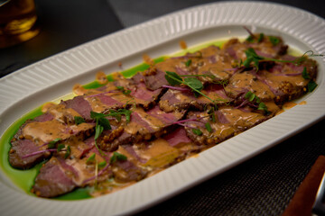 Deliciously prepared gourmet dish featuring tender slices of meat adorned with rich sauce and garnished with fresh herbs, served on an elegant platter.