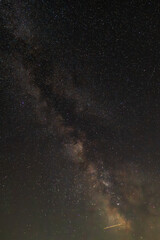 Against a dense field of stars and the glowing path of the Milky Way, a single streak cuts through—like a whispered wish flung across the dark canvas of eternity