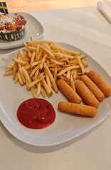Plate with crispy french fries, breaded cheese sticks and a serving of ketchup on a white table