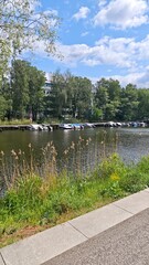Sunny canal scene with moored boats, lush greenery and a clear blue sky in a peaceful urban area....