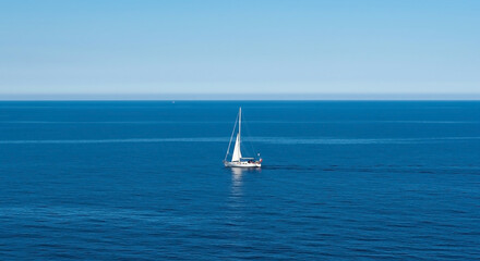 Fototapeta premium A solitary white sailboat cruises across the calm deep blue sea under a clear sky, an idyllic scene of summer vacation and peaceful travel.