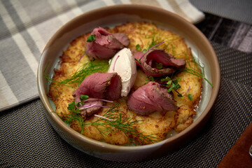 Delectable gourmet dish featuring tender slices of roast meat garnished with fresh herbs on a bed of creamy mashed potatoes served in an elegant bowl.