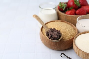 Different ingredients for panna cotta. Milk, sugar, vanilla, chocolate and strawberries on white tiled table, closeup. Space for text