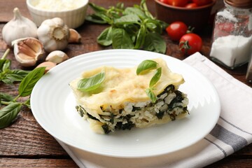 Piece of tasty vegetarian lasagna and ingredients on wooden table, closeup