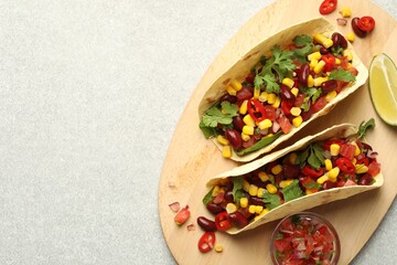 Tasty vegetarian tacos with beans, vegetables and lime on light grey table, top view. Space for text