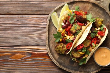 Tasty vegetarian tacos with falafel served with sauce on wooden table, top view. Space for text