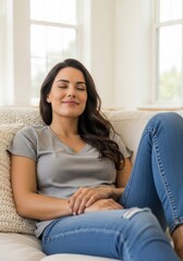 Obraz premium Woman Relaxing on Couch at Home - A young woman in casual wear sits comfortably on a couch, eyes closed, expressing peace and contentment.