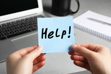 Woman holding paper note with word Help at workplace, closeup