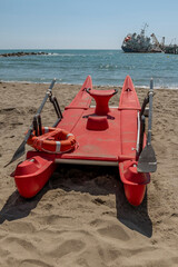 A red lifeboat with a ship tilted after hitting the pier in the background, Marina di Massa, Italy