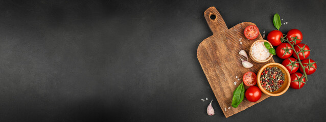 Rustic wooden cutting board with fresh tomatoes, herbs, garlic, salt, and pepper on black...