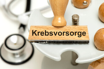 Ein Holzstempel ist beschriftet mit dem Aufdruck Krebsvorsorge und liegt symbolisch über einem...
