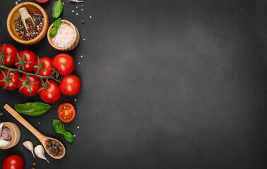 Fresh tomatoes, herbs, garlic, and spices arranged on black background with copy space. top view.